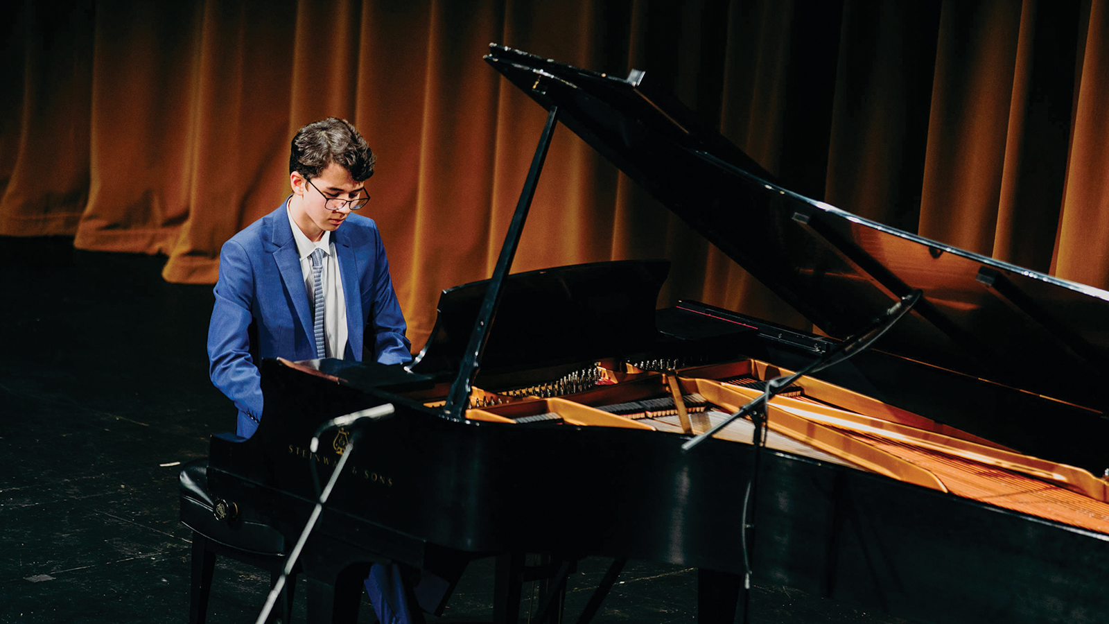 person in a blue suit playing a black piano